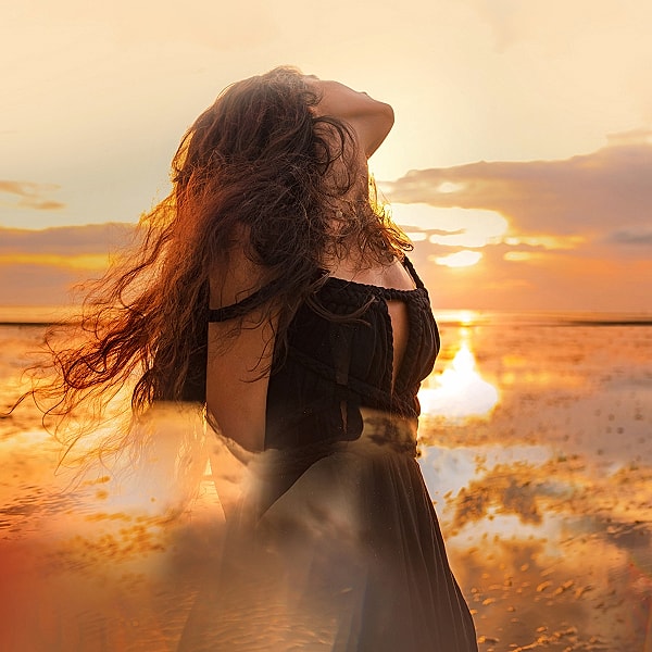 Woman in black dress against sunset backdrop.