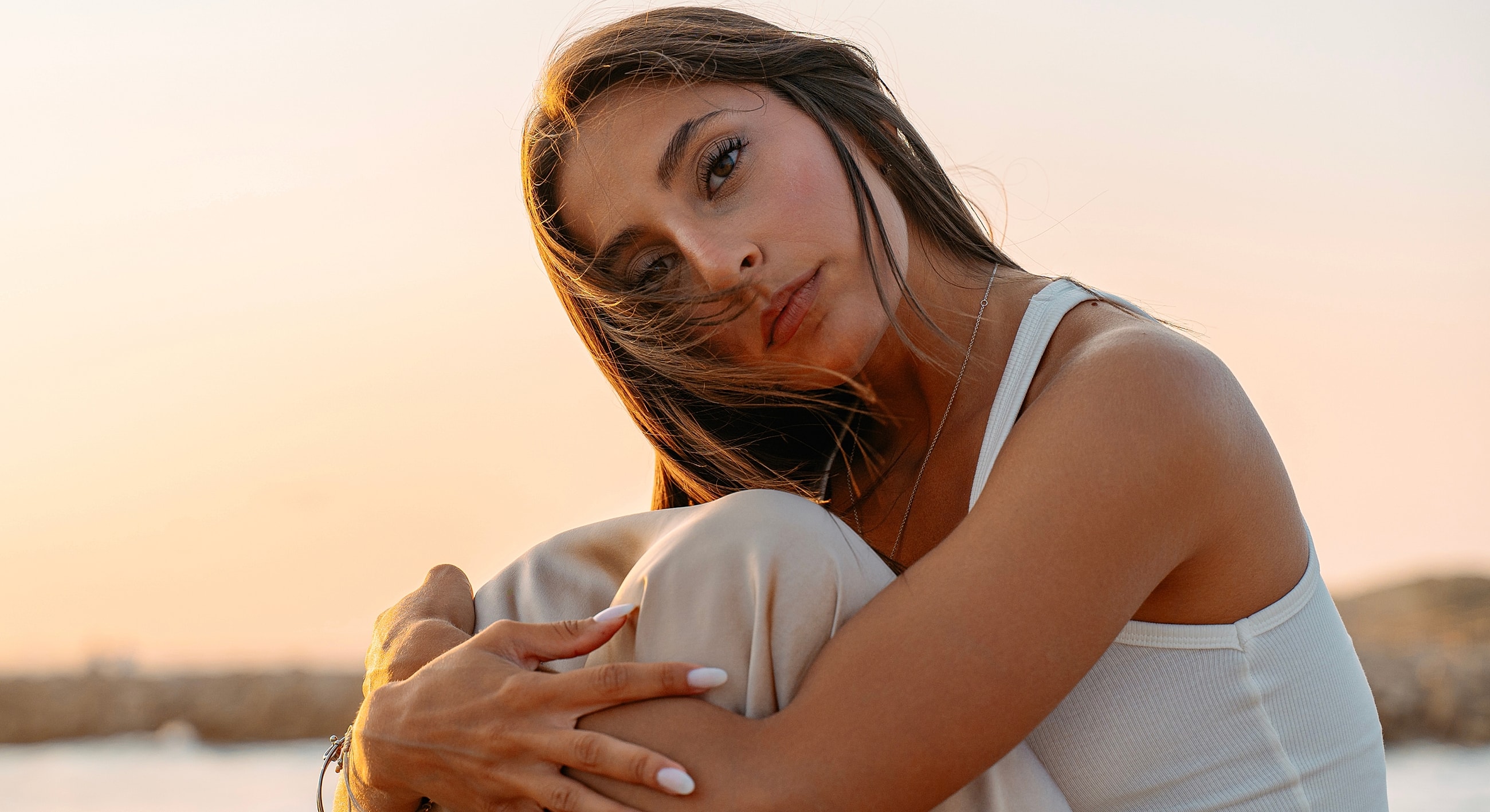 Woman sitting outdoors, sunset in background.
