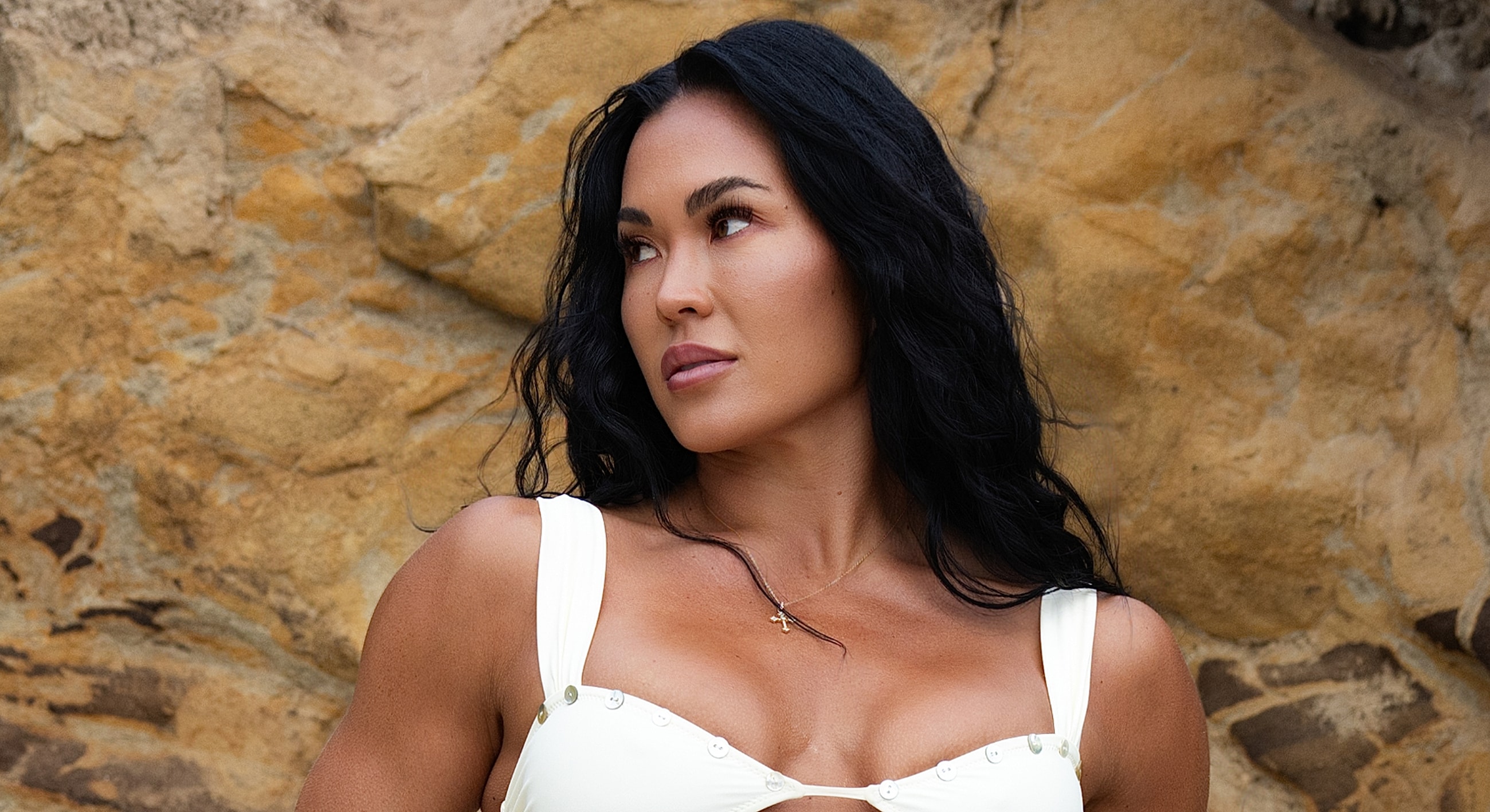 Woman in a white top against rocky background.
